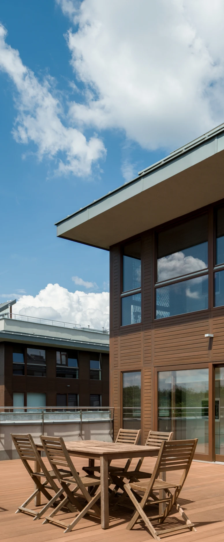 Wooden patio furniture on modern building rooftop.